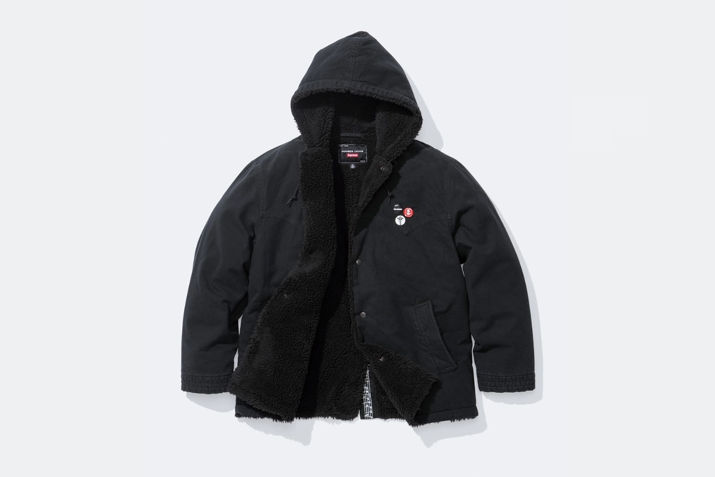 veste noire Supreme x Number (N)ine ouverte avec doublure en fourrure et capuche sur fond blanc