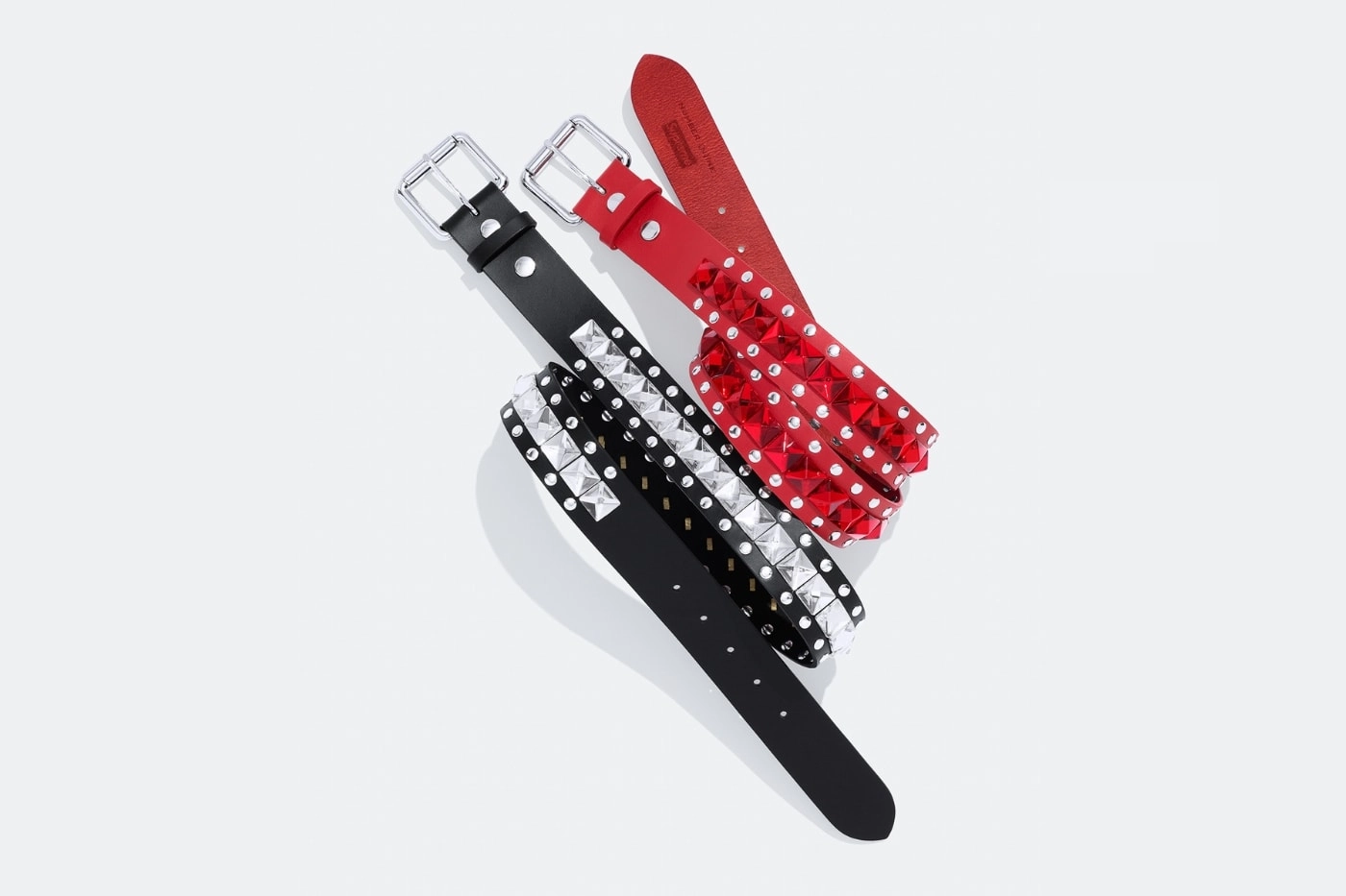 ceintures rouges et noires Supreme Number N(I)ne avec clous argentés sur fond blanc