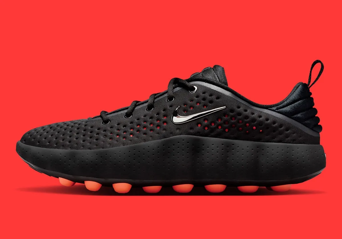 Profil latéral gauche de sneaker Nike noire avec Swoosh chrome sur fond rouge