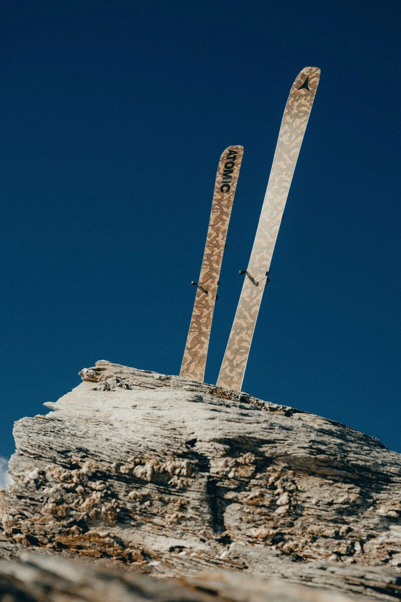 Pair of Atomic Grottoflage 2025 skis planted in a rock under a blue sky