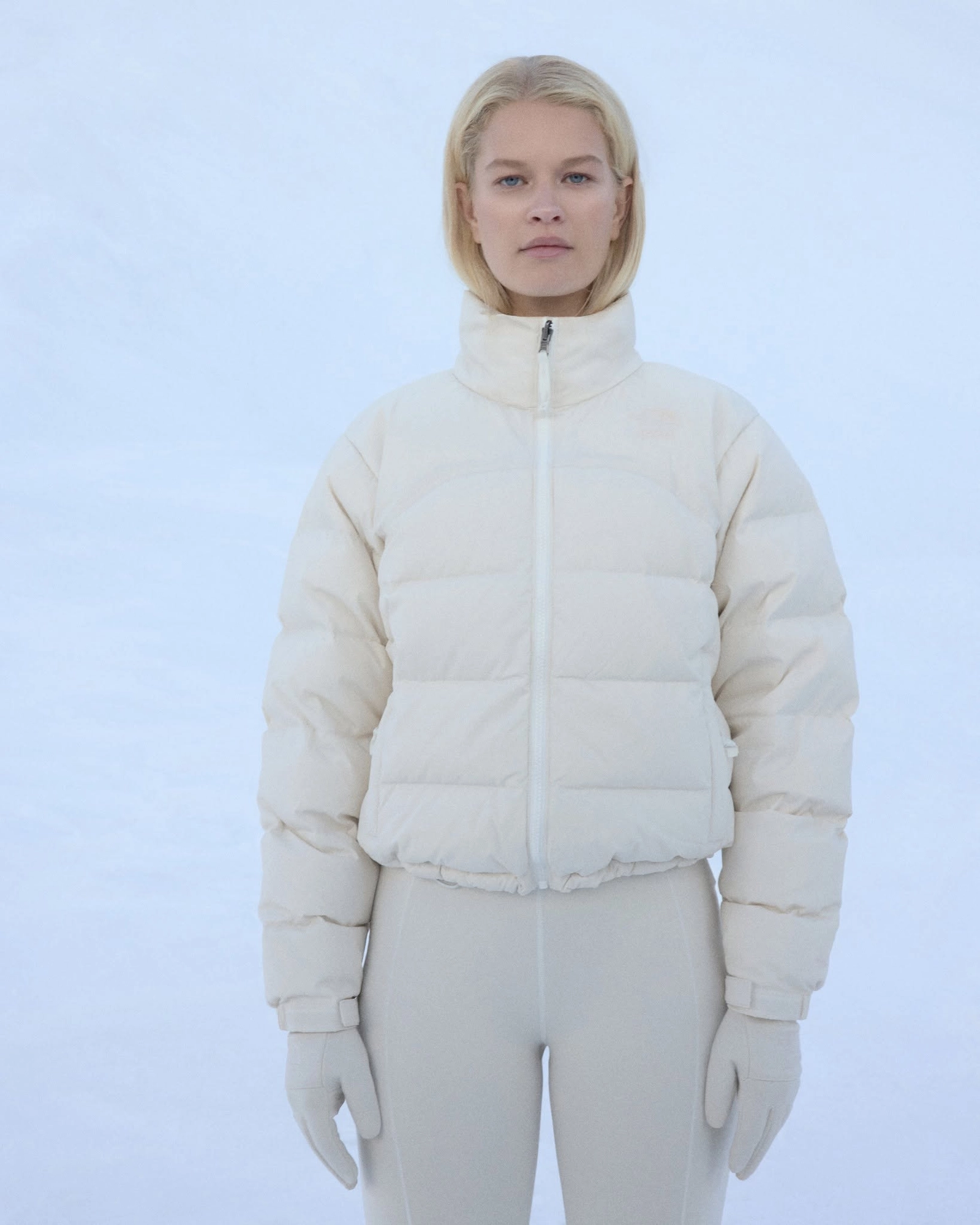 Model wearing a white The North Face x Skims down jacket facing the camera against a snowy background