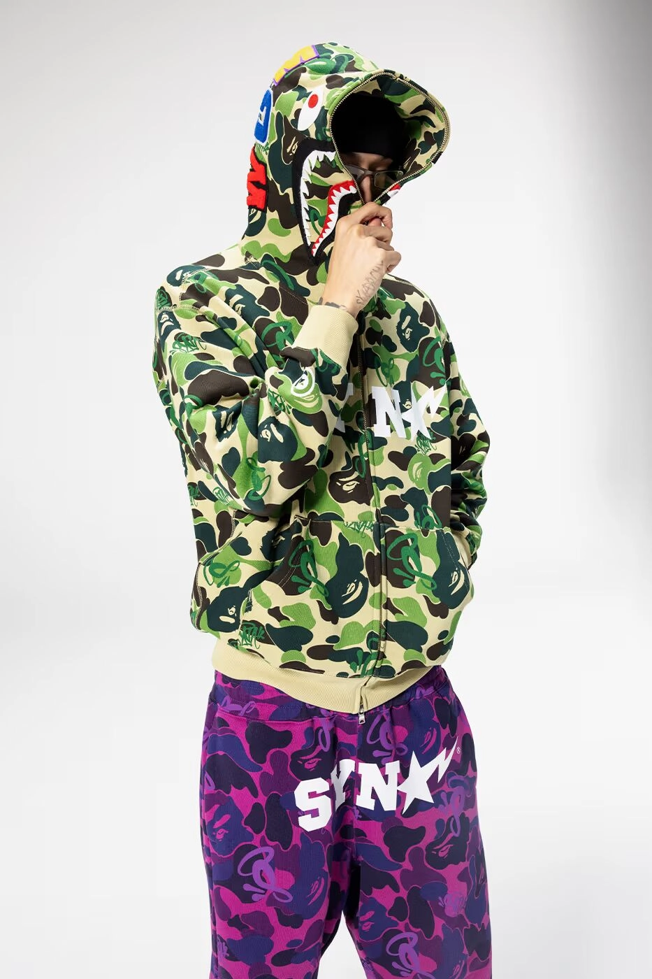 Person wearing a BAPE camouflage jacket with shark hood, neutral background