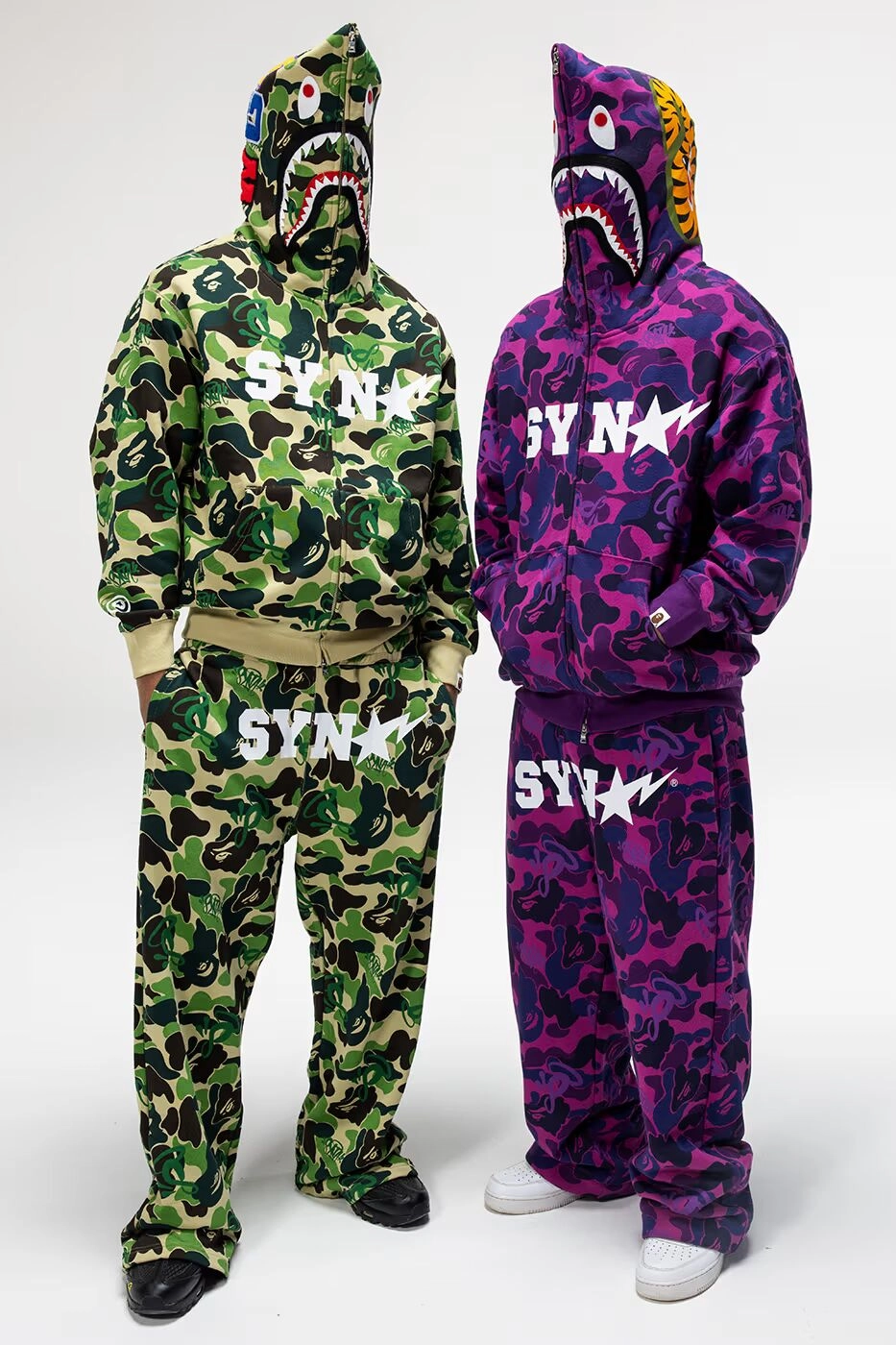 Two people wearing green and purple BAPE x Syna hoodies on white background