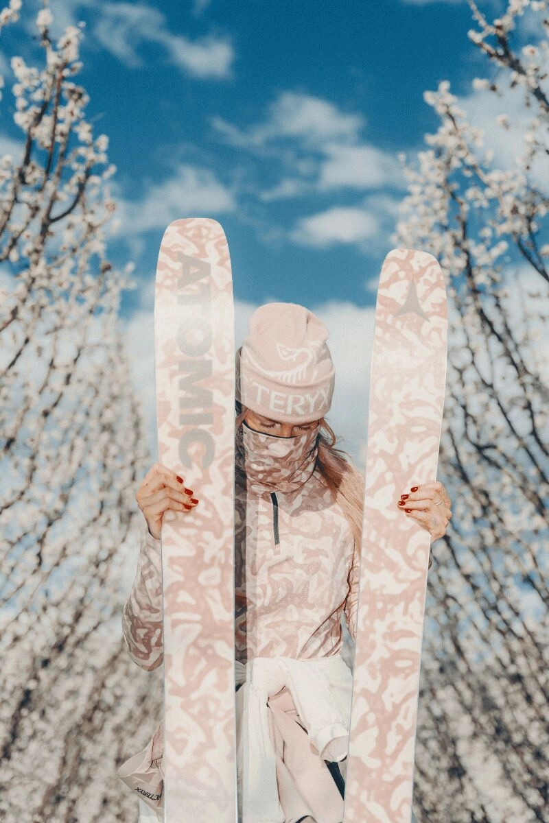 Person with Atomic Grottoflage skis and Arc'teryx x Atomic outfit under a blue sky