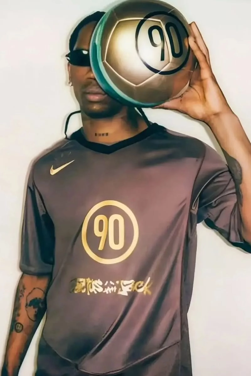 Travis Scott with the golden Cactus Jack x Nike Total 90 ball in front of his face, brown jersey visible
