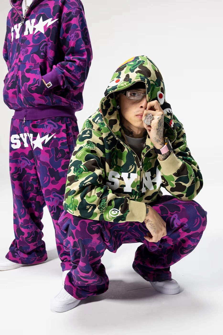 Modèle portant une tenue camouflage vert et violet SYNA par Central Cee x Bape