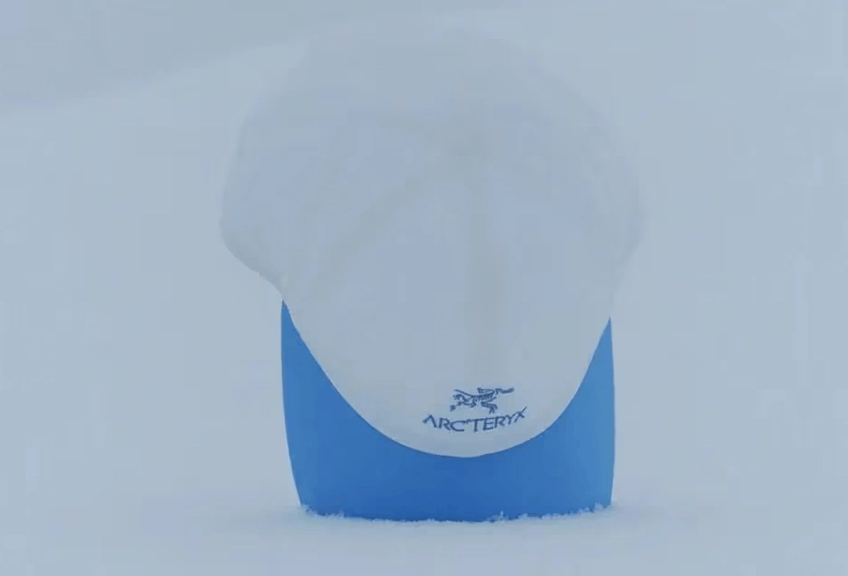 casquette Arc'teryx blanche avec visière bleue sur fond enneigé